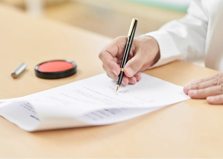 契約書に署名している様子。机の上には朱肉と印鑑が置かれている